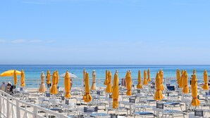 A beach with rows of sun loungers and yellow umbrellas, a clear blue sky, and the ocean in the background.