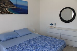 Un dormitorio con cama, cómoda, espejo y un cuadro de un paisaje costero.