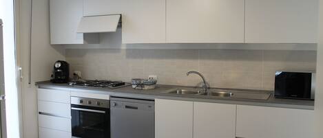 Een moderne keuken met witte kasten, roestvrijstalen apparatuur, een vaatwasser en een inbouwmagnetron.