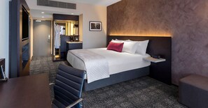 Una habitación de hotel con una cama grande, un escritorio, una silla, una bata y un espejo.