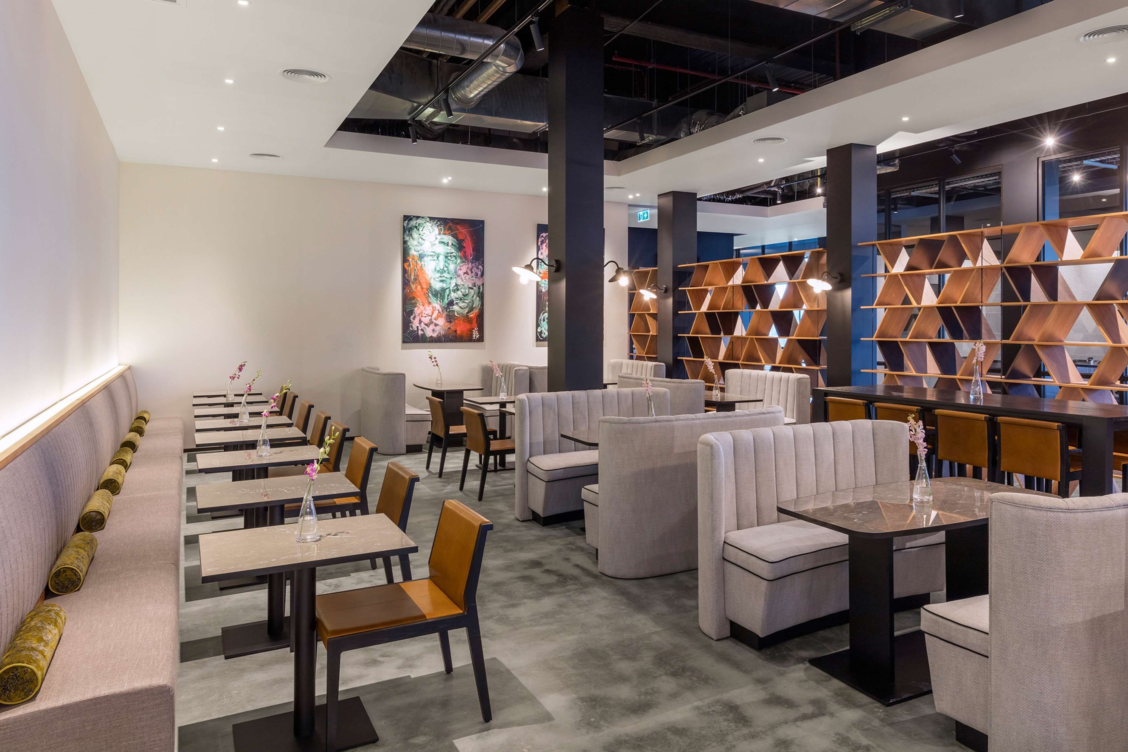 Un restaurant moderne avec des tables hautes et des banquettes, une grande peinture abstraite au mur et un meuble de rangement en bois au design original.