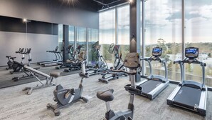 A gym with various exercise equipment, large windows, and a view of the outdoors.