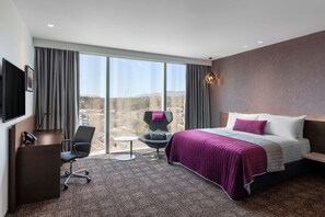 Habitación de hotel moderna con una cama grande, un escritorio, una silla y vistas a la ciudad.