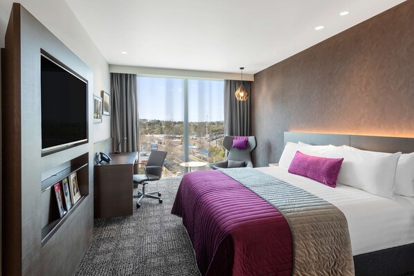Habitación de hotel con una cama grande, un escritorio, un televisor de pantalla plana, una silla y vistas a la ciudad.