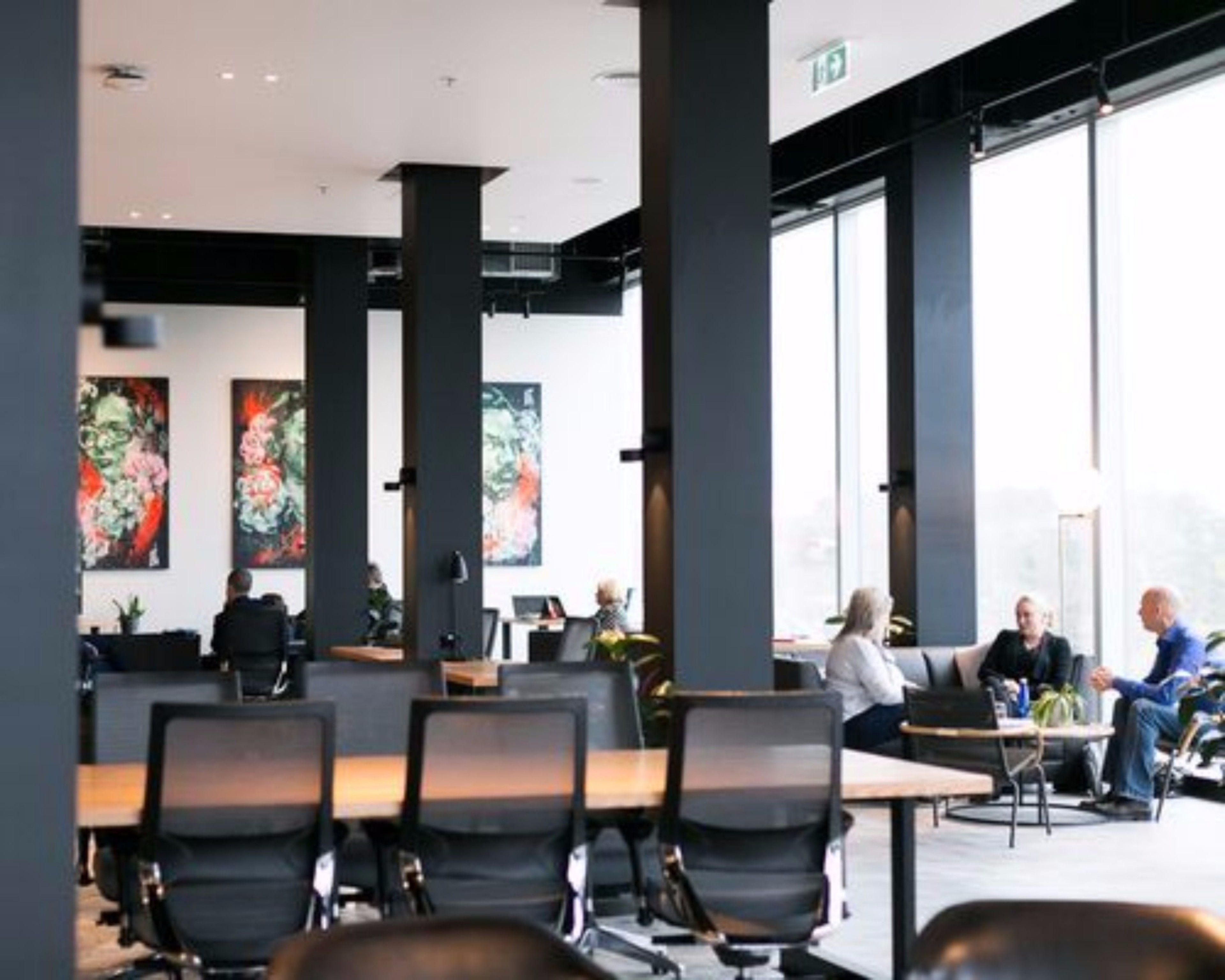 A modern office space with large windows, black chairs, and artwork on the walls.