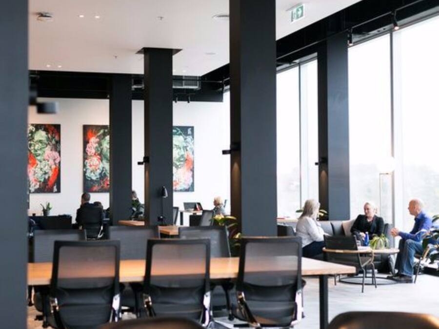 A modern office space with large windows, black chairs, and artwork on the walls.