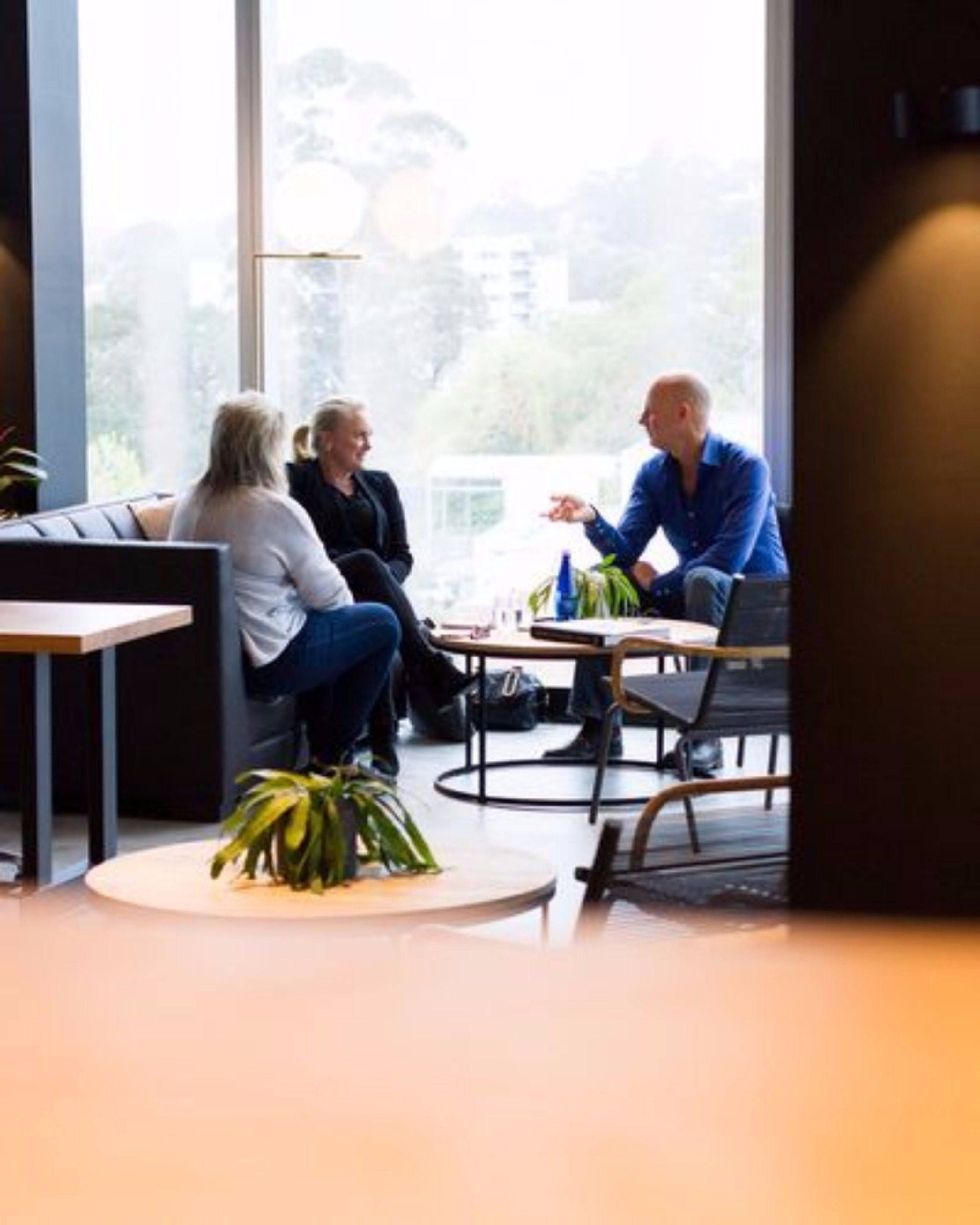 A modern meeting room with large windows, a round table, and a sofa.