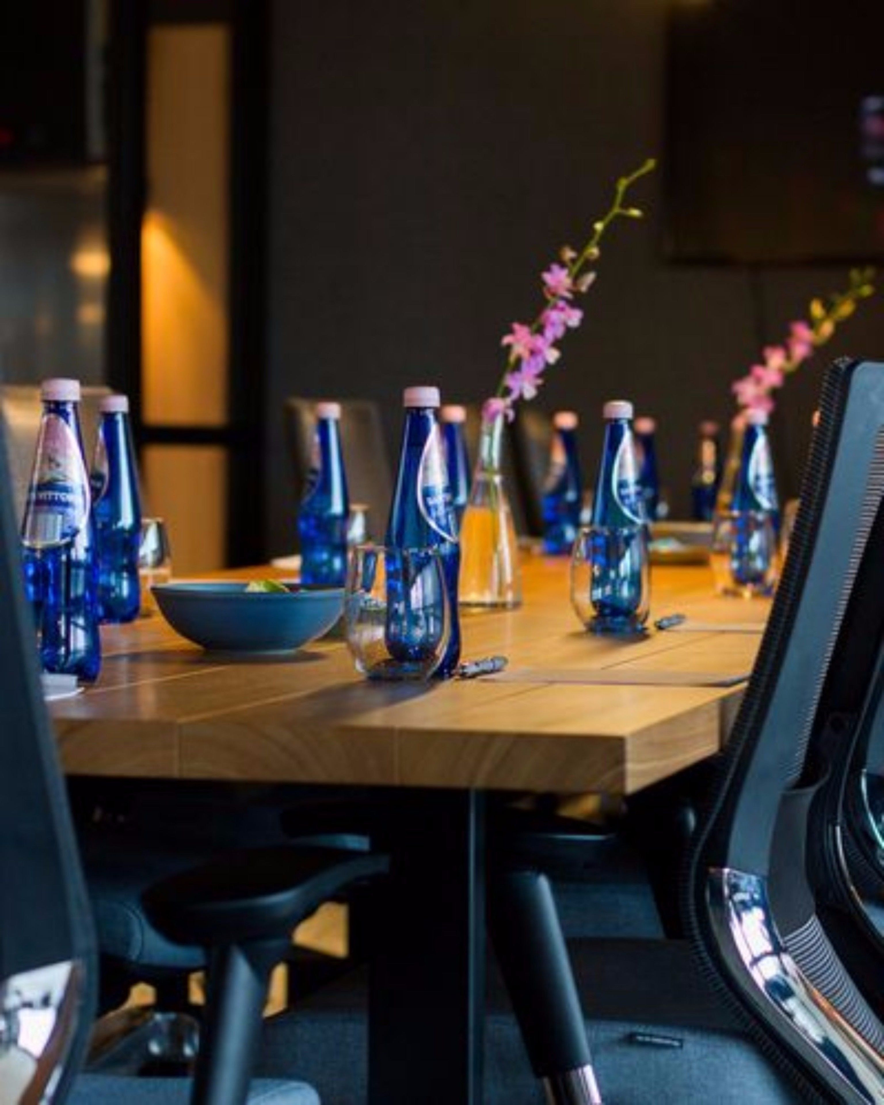 A conference table with blue water bottles, a bowl, and a vase with pink flowers.