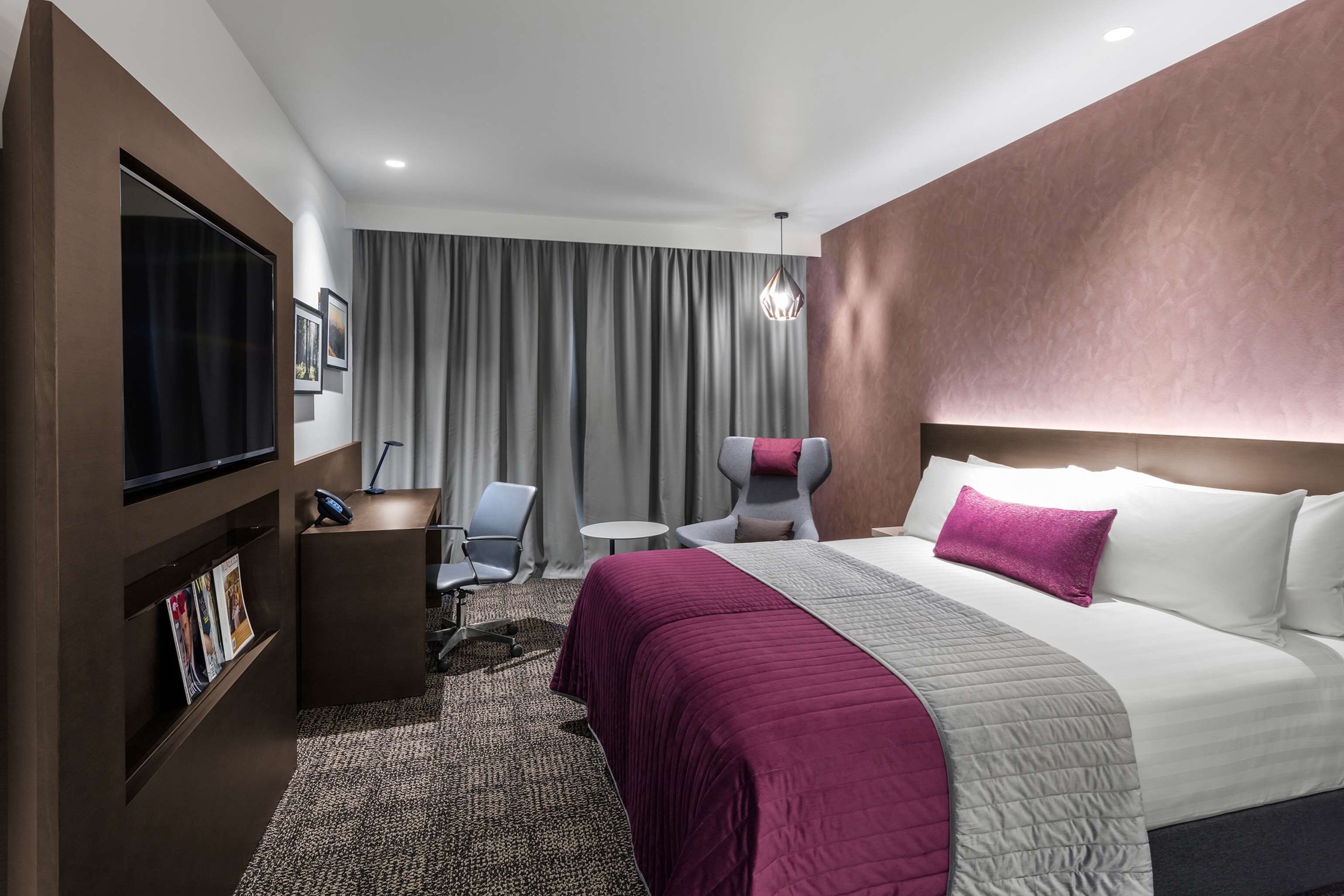 Una habitación de hotel con una cama grande, un escritorio, una silla, un televisor y una estantería.