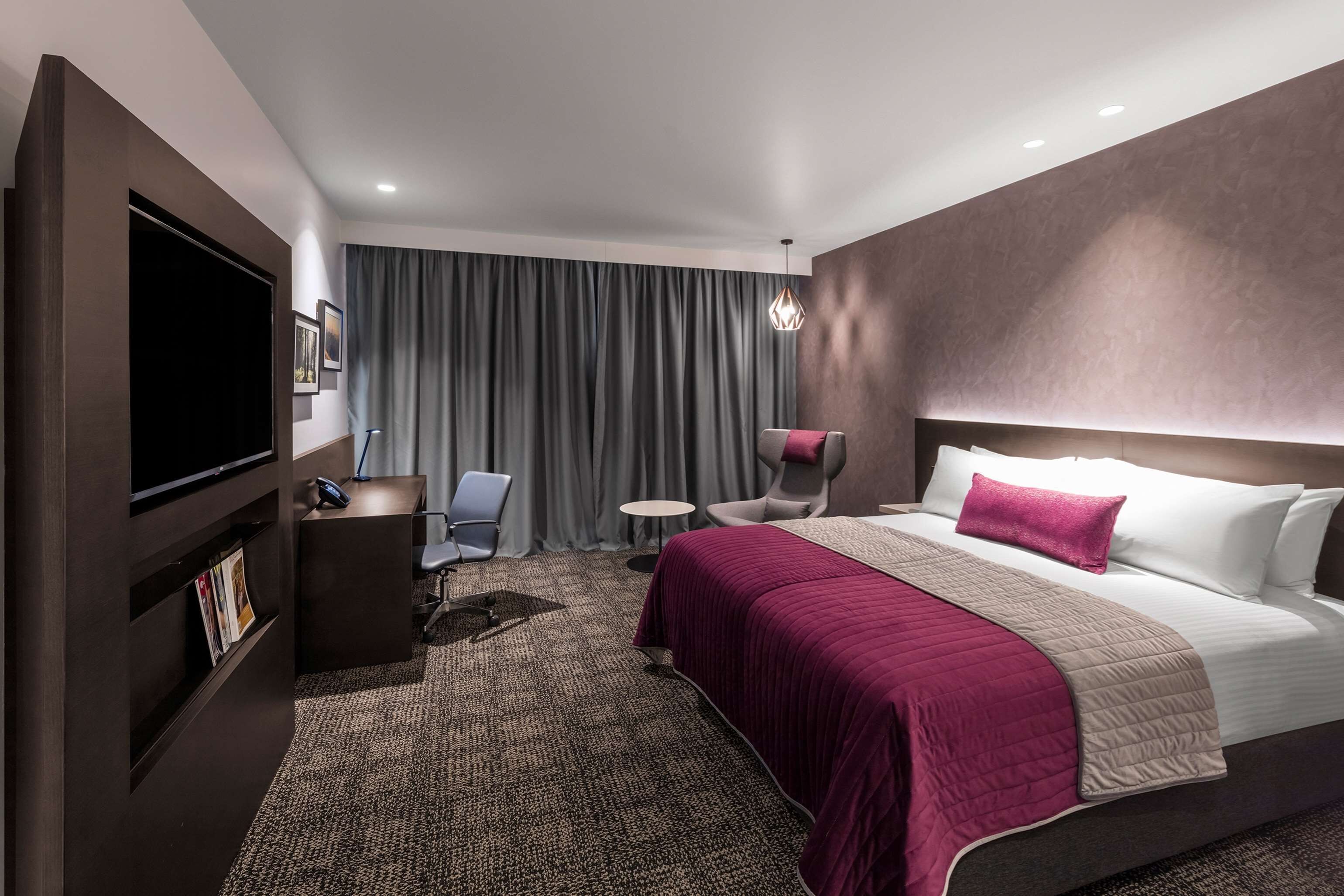 Una habitación de hotel moderna con una cama grande, un escritorio, una silla, un televisor y una mesita.