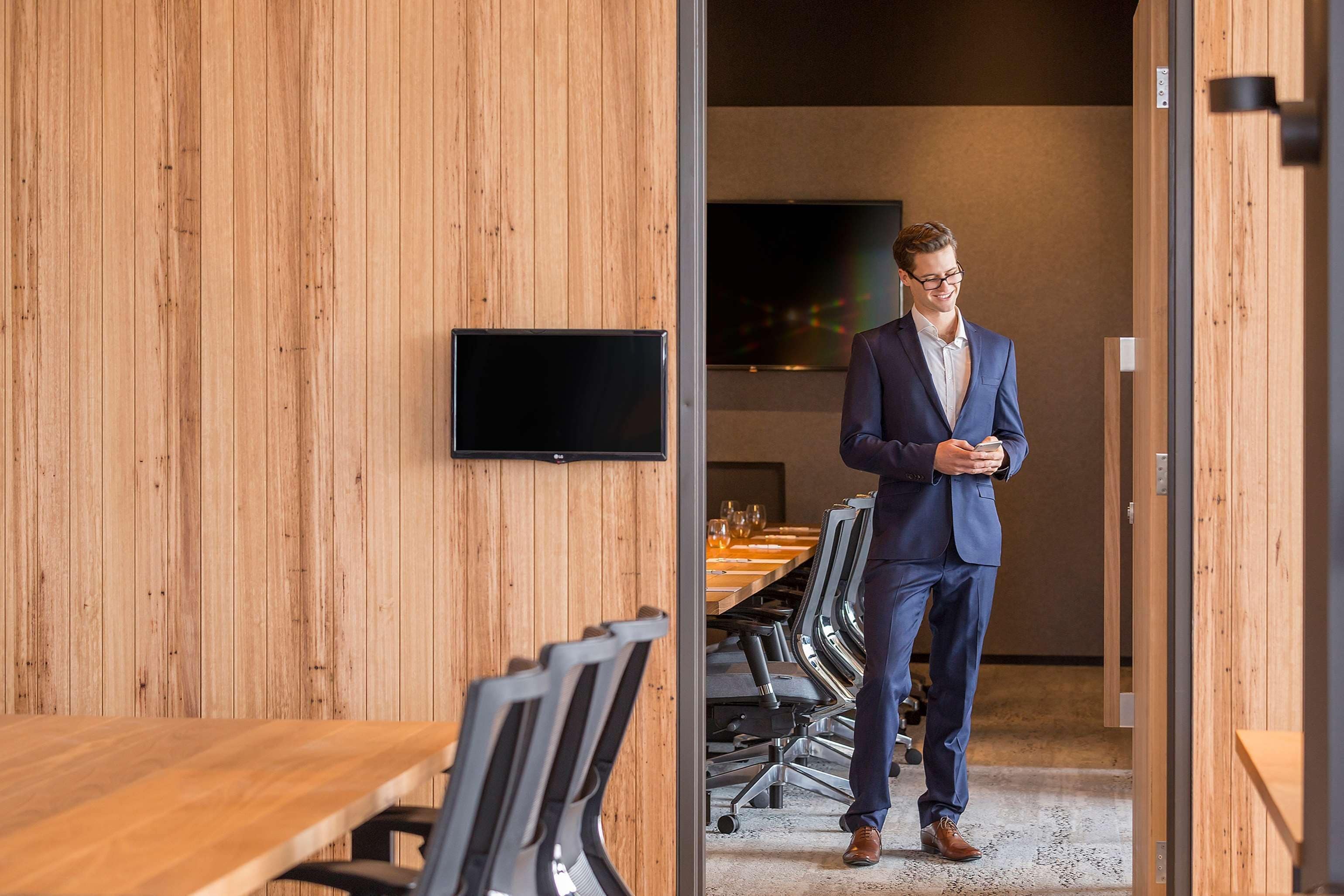 A modern conference room with wooden walls, a large table, and office chairs.