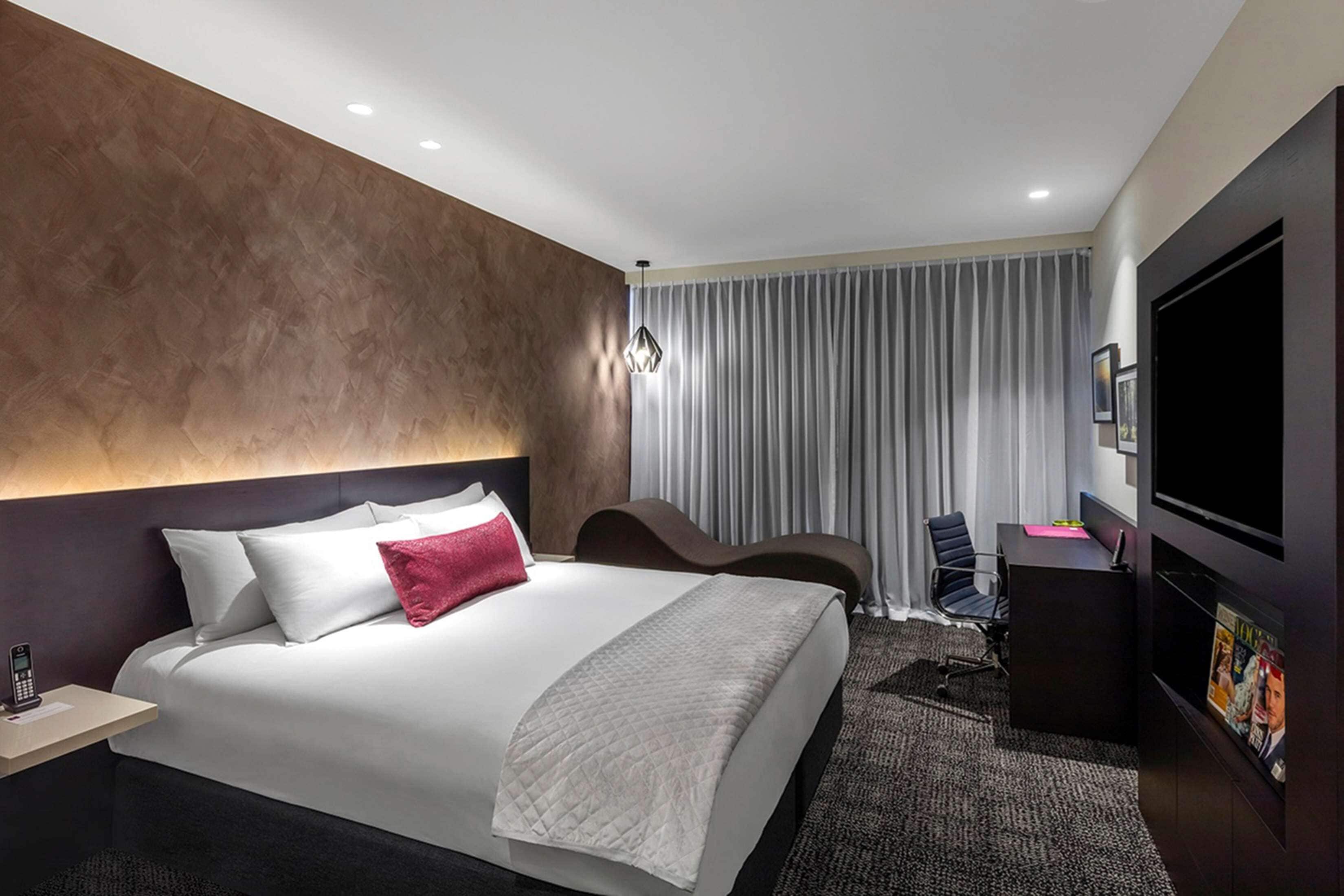 A modern hotel room with a large bed, a desk, a chair, a television, and a curtain.