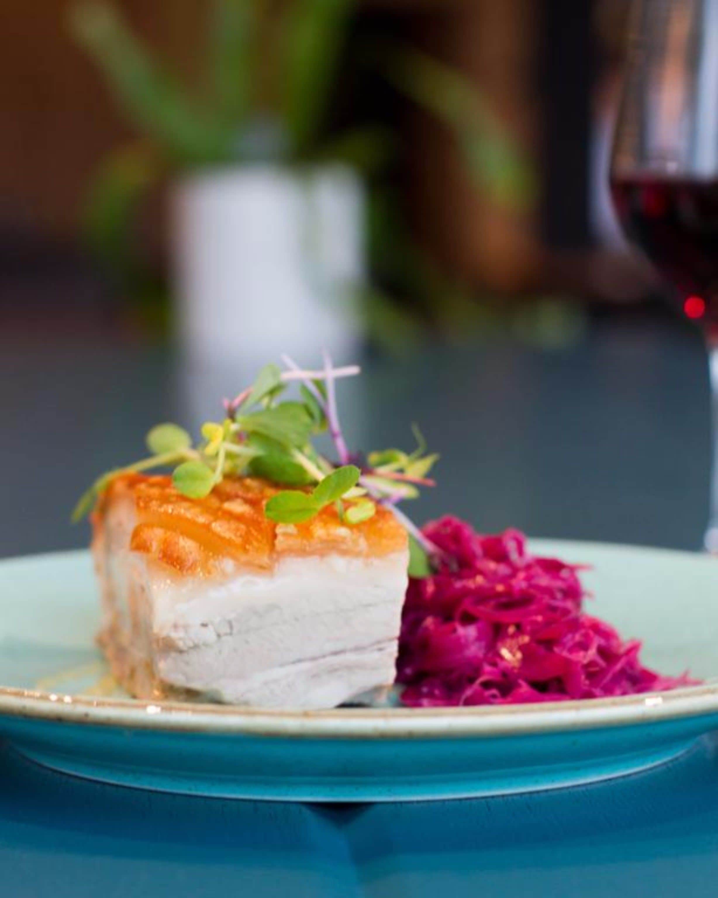 A plate with a piece of food and a glass of red wine on a table.