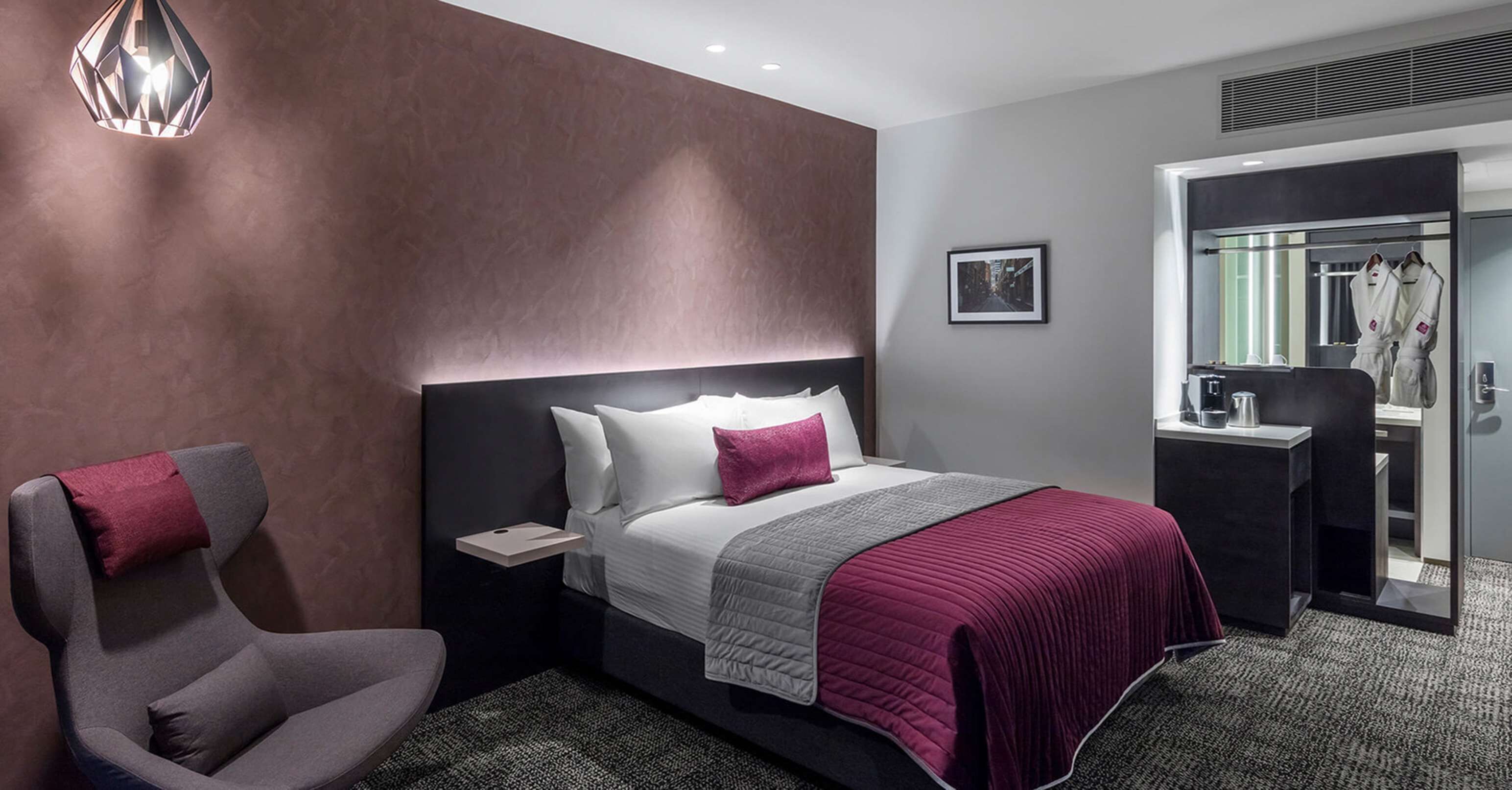 Une chambre d’hôtel moderne avec un grand lit, une table de chevet, une chaise et une armoire.