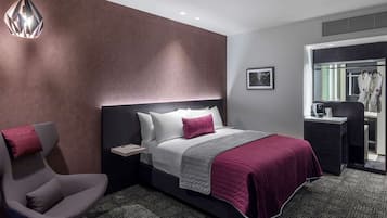 A modern hotel room with a large bed, a bedside table, a chair, and a wardrobe.
