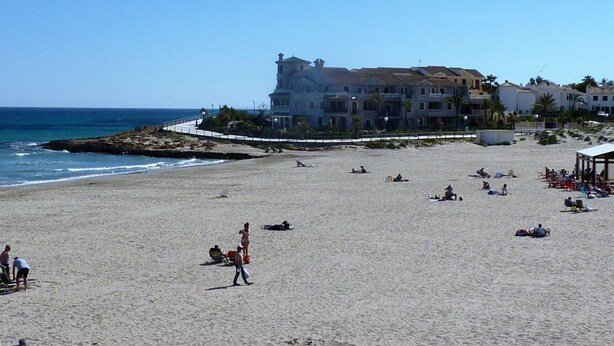 A beach with a large building in the background, a few people on the sand, and the ocean.