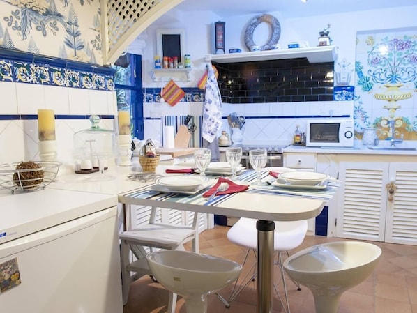 A modern kitchen with a dining area, featuring a white and blue tiled backsplash, a microwave, and a sink.