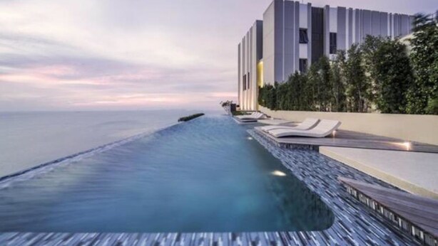 Een modern hotel met een lang, smal overloopzwembad dat uitloopt richting de oceaan, een gebouw met verticale lijnen en een rij ligbedden.