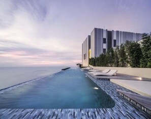 A modern hotel with a long, narrow infinity pool extending to the ocean, a building with vertical lines, and a row of sun loungers. - Baan Plai Haad By Pong (Pattaya)