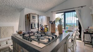 Une cuisine moderne dotée d’un îlot central, d’appareils électroménagers en acier inoxydable et offrant une vue sur la mer grâce à de grandes fenêtres.