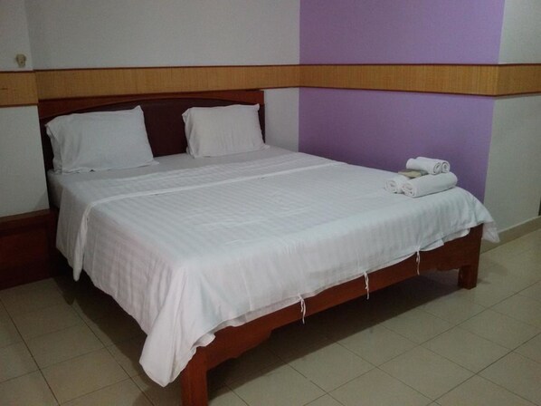A neatly made bed with white linens, a wooden headboard, and a purple accent wall.