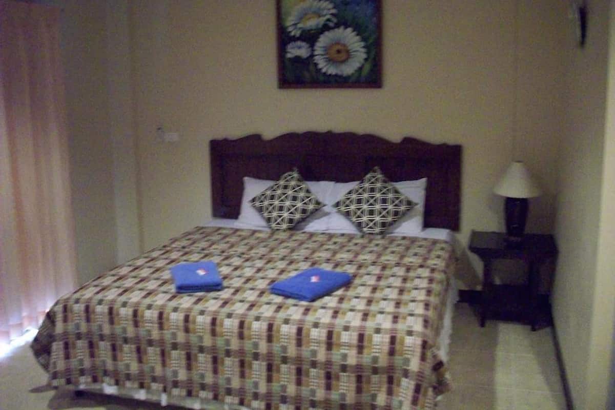 A bedroom with a bed, a painting of flowers, a nightstand, and a lamp.
