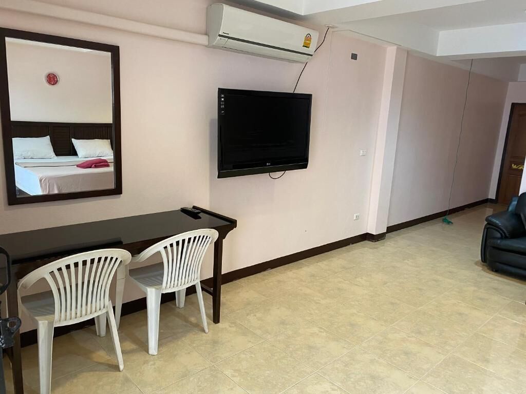 A room with a bed, a TV mounted on the wall, a desk with two chairs, and an air conditioning unit.