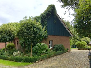 Ein traditionelles Backsteinhaus mit einem steilen Dach, umgeben von üppigem Grün und einem Kopfsteinpflasterweg.