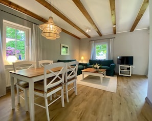 Cozy living space with a dining table, sofa, and TV stand, offering a view of the surrounding greenery.
