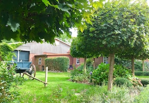 Ein Garten mit einem hölzernen Wagen, einem Haus und einem Baum.