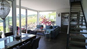 Un salon moderne avec une table à manger en verre, des sièges confortables, un escalier et une vue sur l’extérieur.