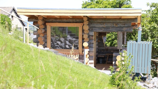 Une cabane en rondins avec un porche en bois et une fenêtre équipée de stores.