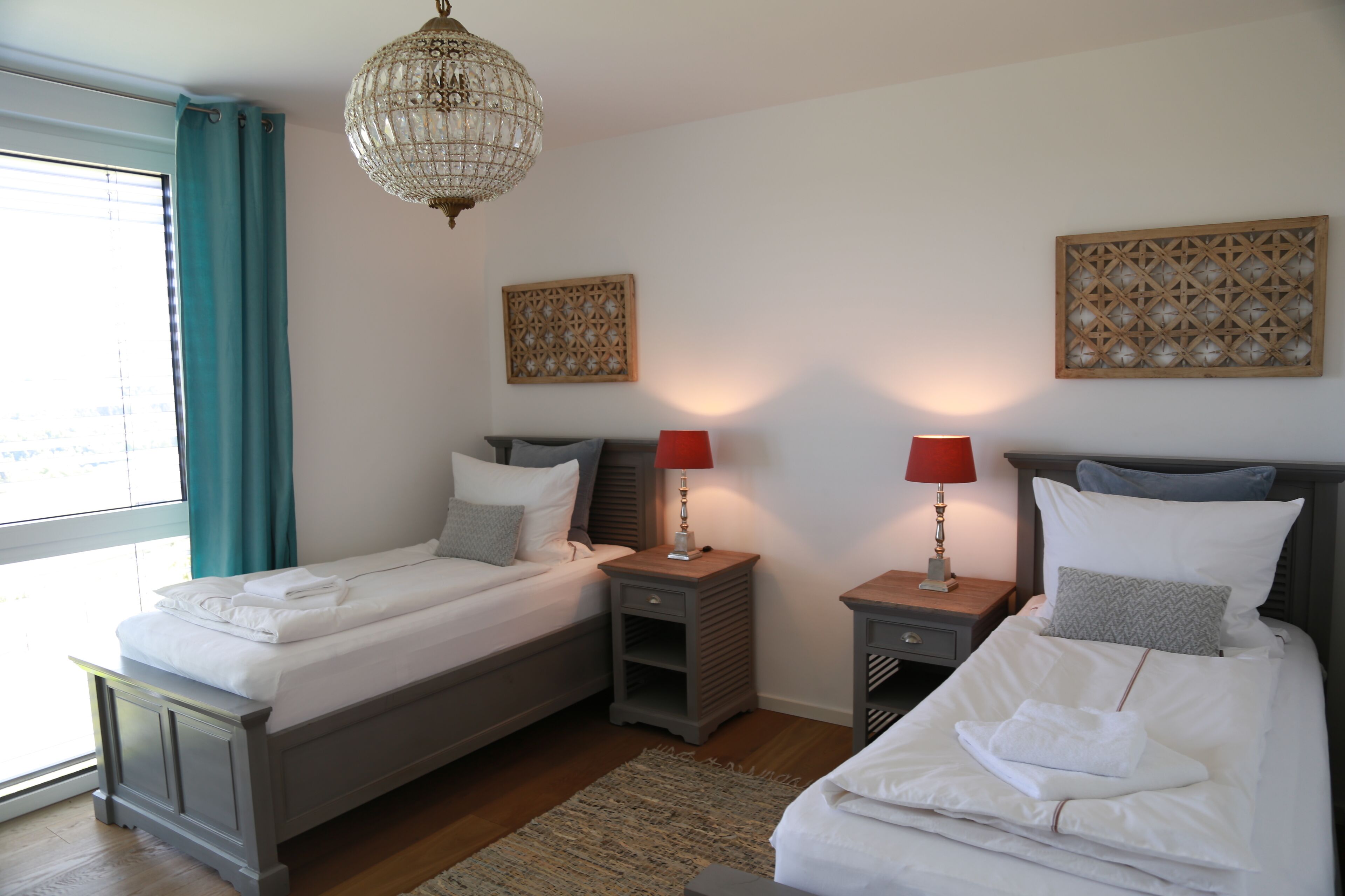 A hotel room with two beds, a chandelier, decorative wall panels, and a view of the outdoors.