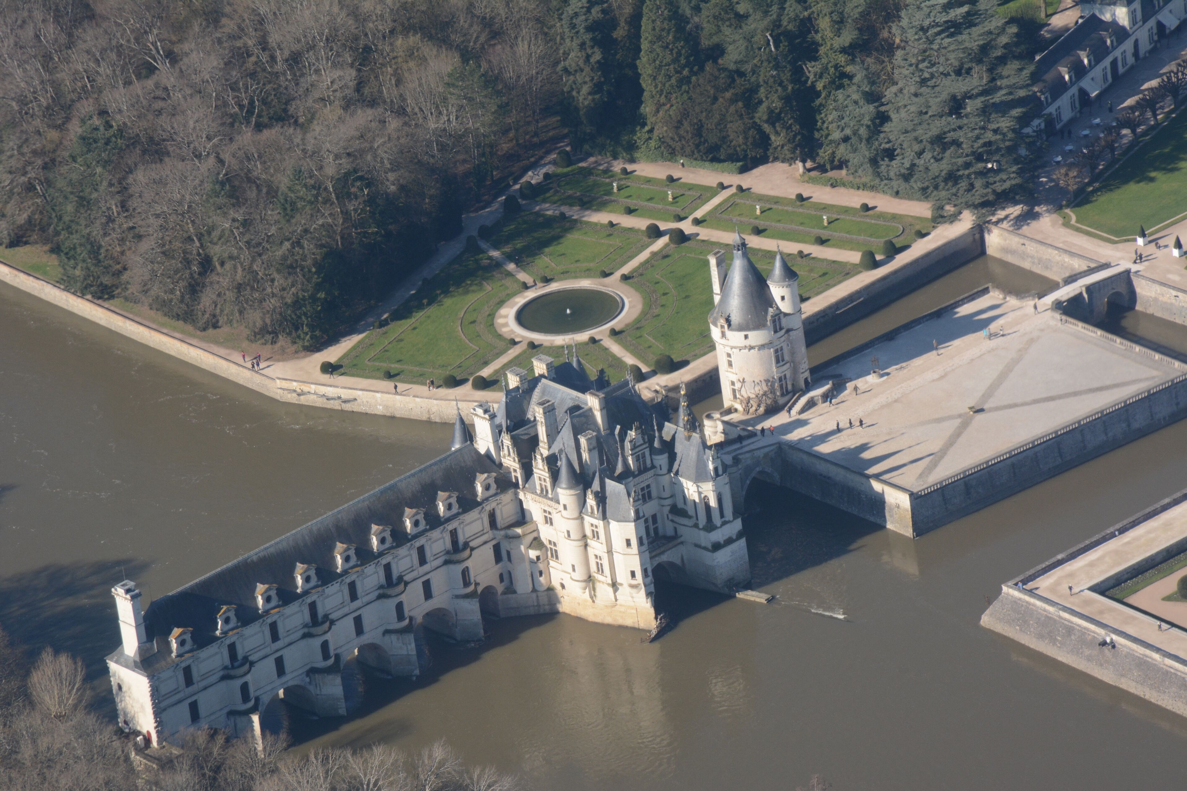 An aerial view of a castle with a moat, a round garden, and a bridge connecting to the mainland.