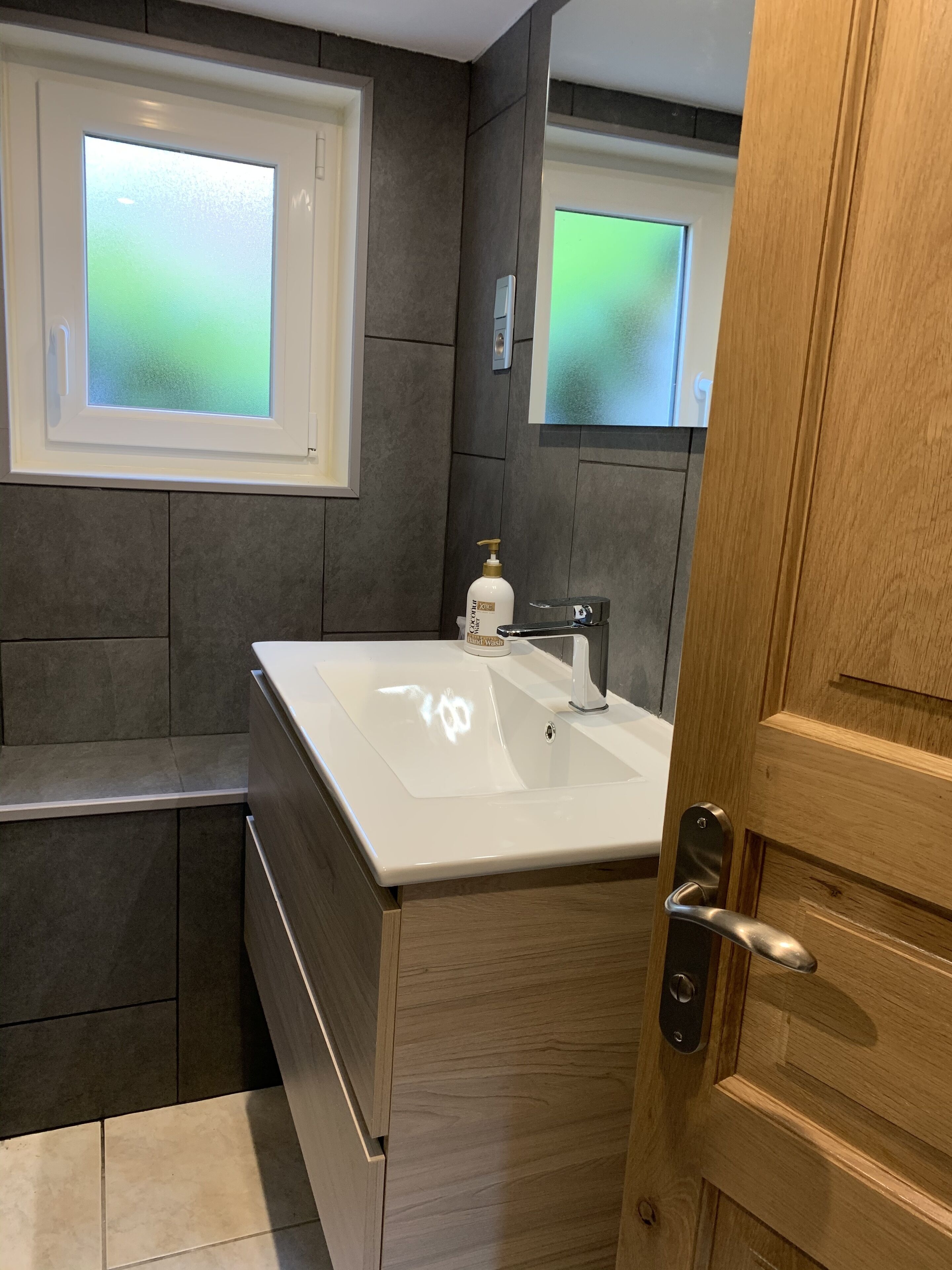 Un baño moderno con un lavamanos grande, un espejo y un ventanal esmerilado.