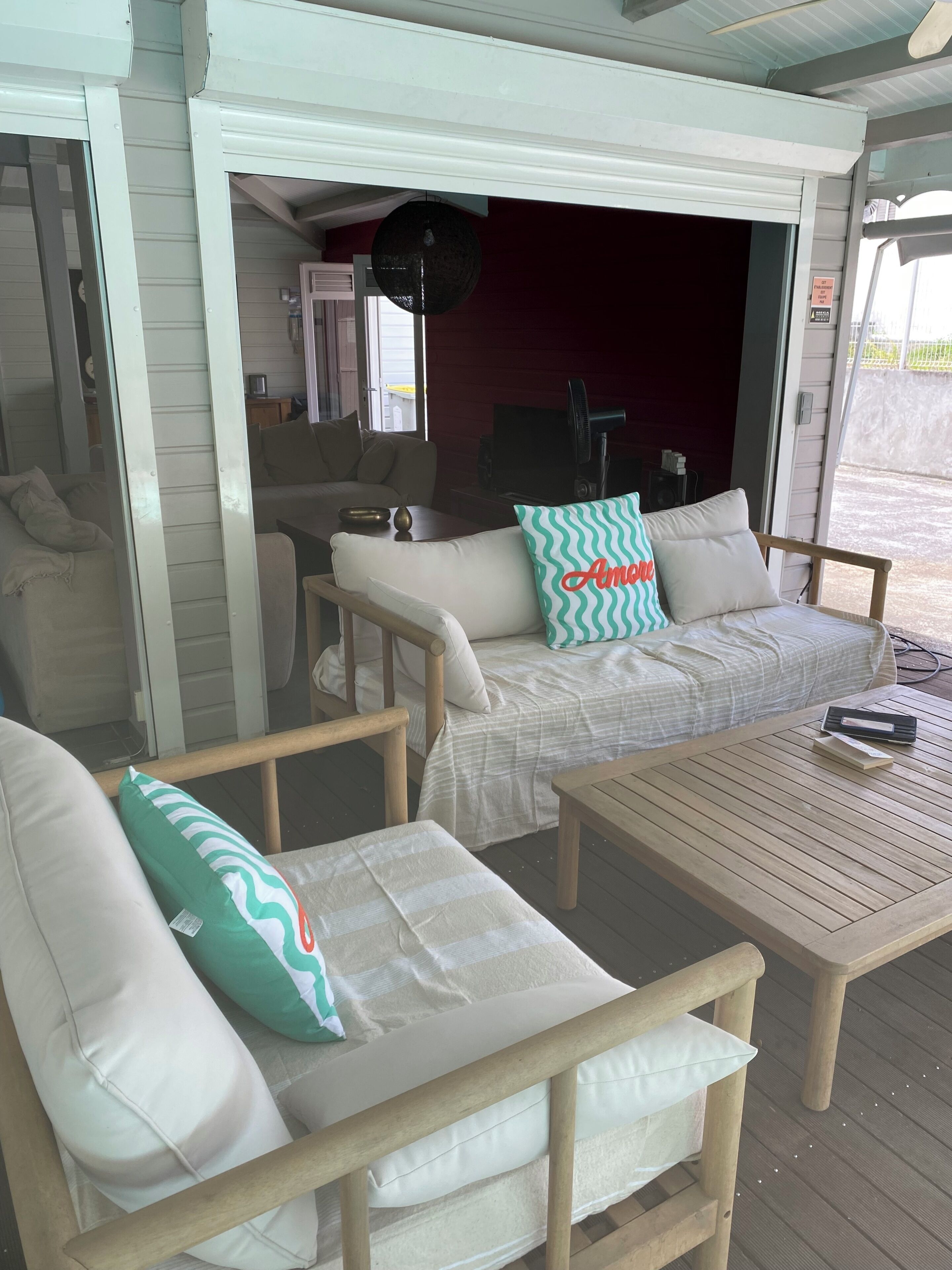 A covered outdoor seating area with a wooden table and two sofas with cushions.