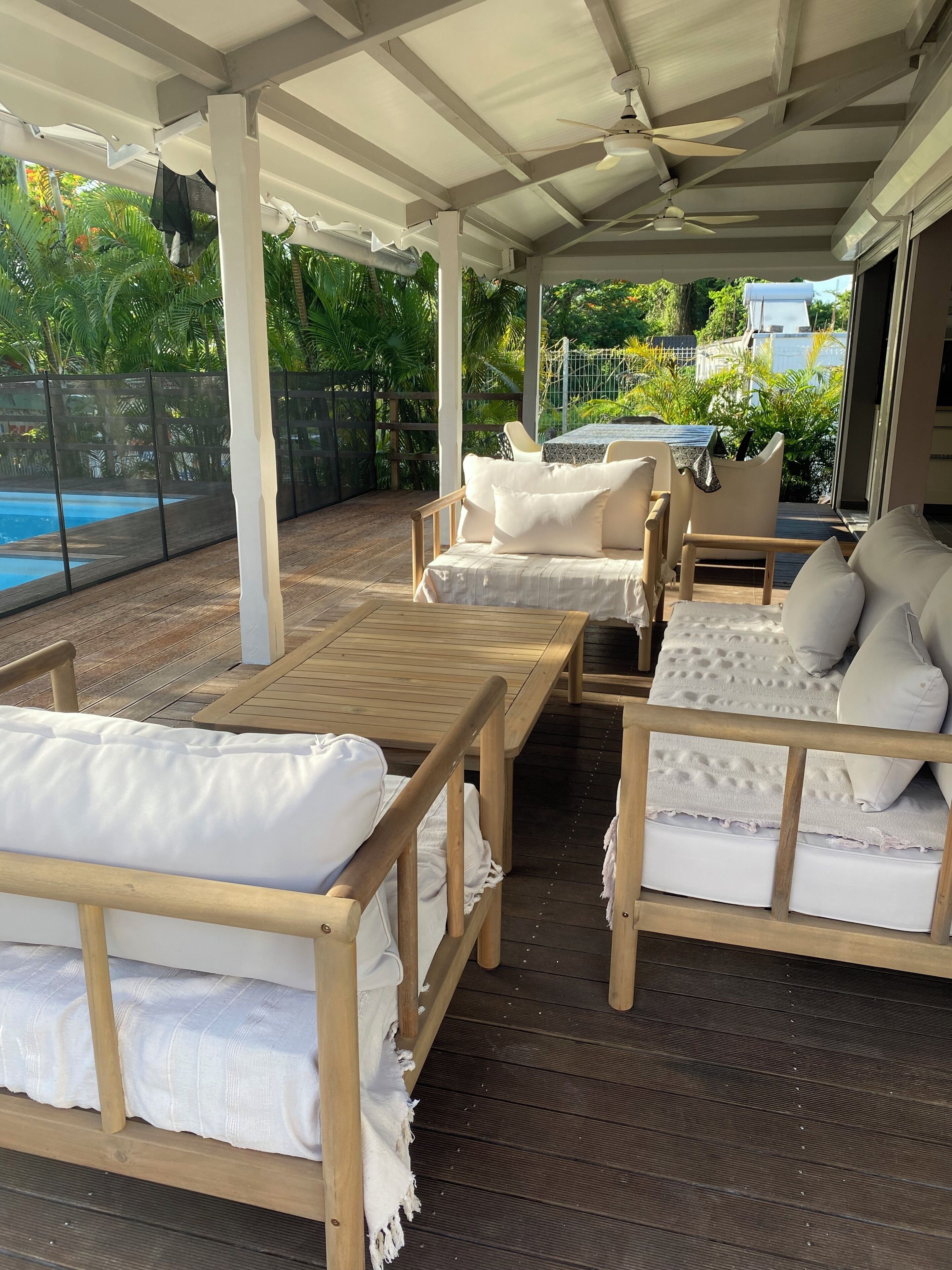 A covered outdoor seating area with wooden furniture and a pool in the background.