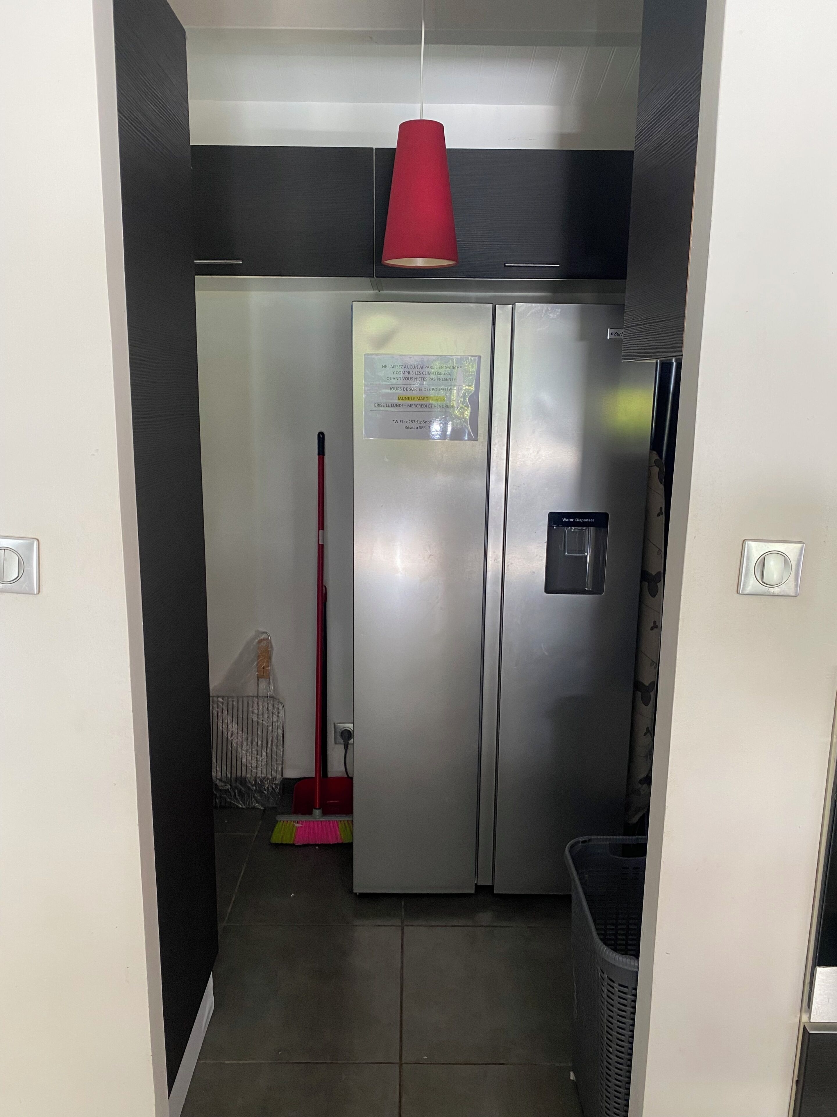 A kitchen with a stainless steel refrigerator, a red hanging light, and a water dispenser.