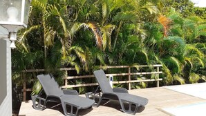 Two lounge chairs by a poolside with a wooden fence and lush greenery in the background. - Cozy and modern charming villa 5 minutes walk from the beach (Le Gosier)