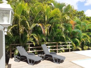 Two lounge chairs by a poolside with a wooden fence and lush greenery in the background.
