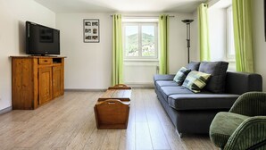 Un soggiorno con televisione, mobiletti in legno, divano e vista sul verde.