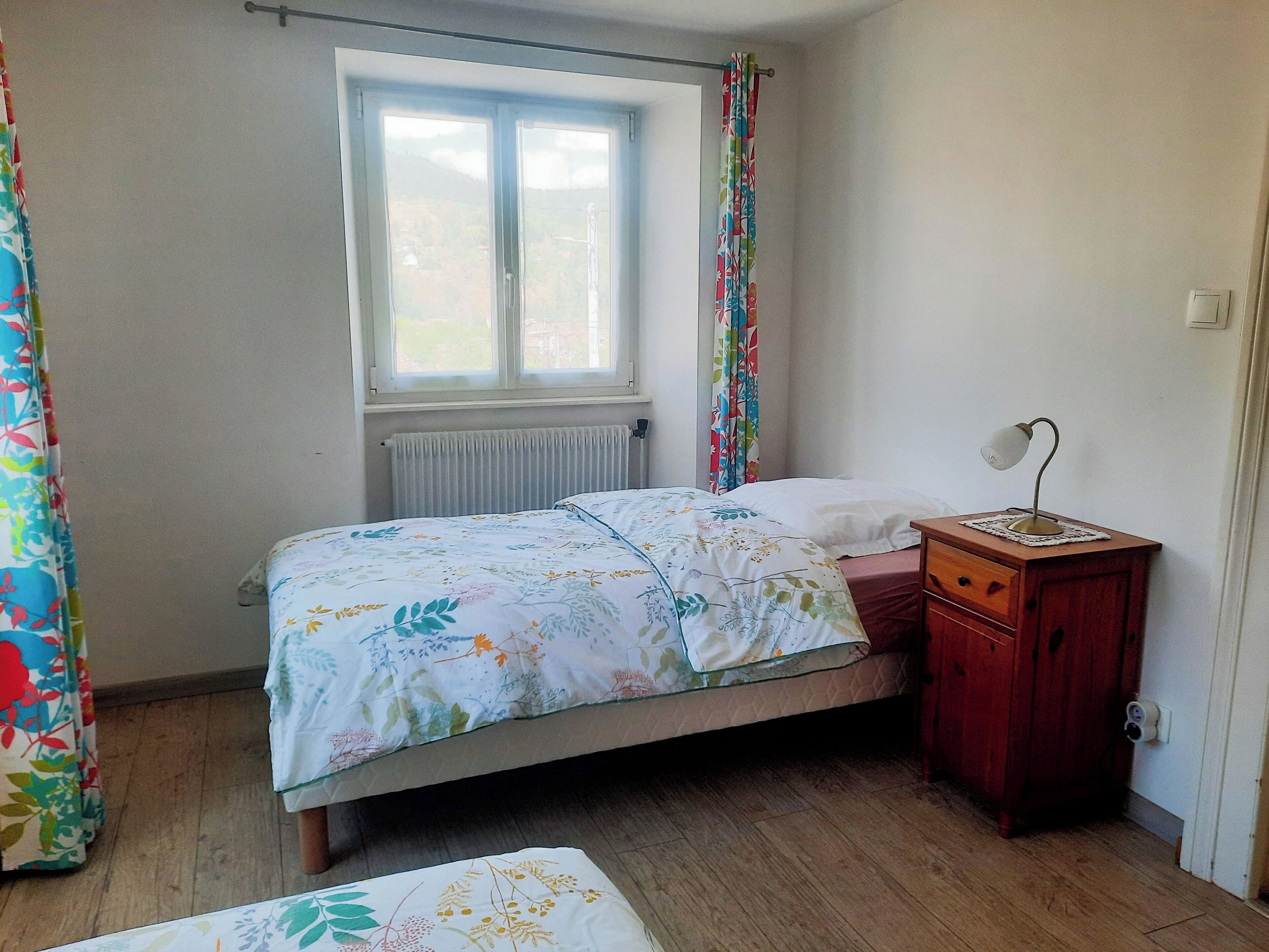 Een slaapkamer met een bed, nachtkastje, raam en radiator.