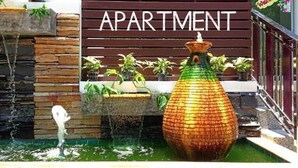 Een bord met de tekst 'BRIGHT APARTMENT', een gevel van steen en hout, een grote decoratieve vaas en potplanten.