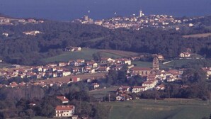 En kystby med en blanding af boliger og erhvervsbygninger, et markant kirketårn og et fyrtårn i det fjerne.