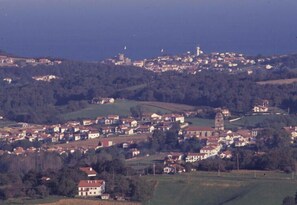 Une ville côtière où se côtoient des bâtiments résidentiels et commerciaux, avec un clocher d’église imposant et un phare visible au loin.