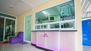 A reception area with a purple chair, a reception desk with a logo, and a glass window displaying a building and contact numbers. - Sritrang Place (Hat Yai)