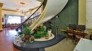 A grand lobby with a curved staircase, a seating area with chairs, and a desk with two monitors. - The Spring Hotel (Ho Chi Minh City)