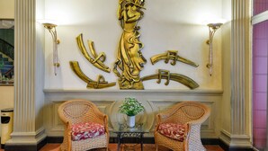 A lobby with two wicker chairs, a small table with a vase, and a large golden sculpture. - The Spring Hotel (Ho Chi Minh City)