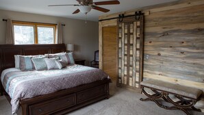 A bedroom with a large bed, a wooden bench, a ceiling fan, and a sliding barn-style door.
