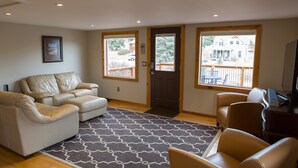 A living room with a beige sofa, a patterned rug, and a view of a backyard through large windows.
